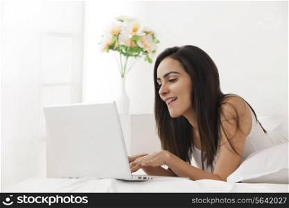 Beautiful young woman using laptop in bed