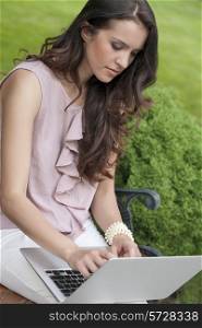 Beautiful young woman using laptop on bench in park