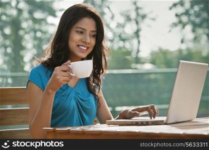 Beautiful young woman using laptop while having coffee