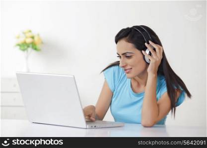 Beautiful young woman using laptop while listening to headphones at home