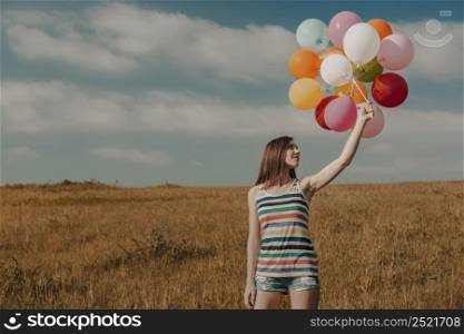 Beautiful young woman walking on meadow holding ballons