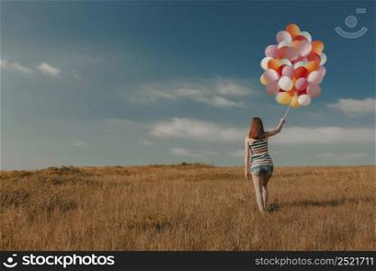 Beautiful young woman walking on meadow holding ballons