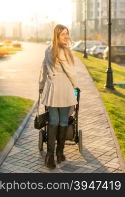 Beautiful young woman walking with baby stroller at park