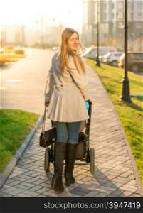 Beautiful young woman walking with baby stroller at park