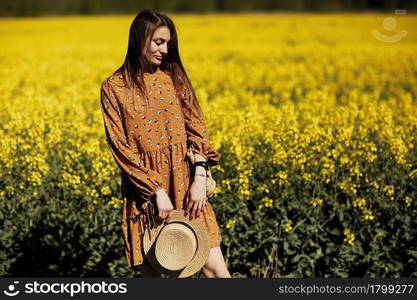 beautiful young woman walks in a field of yellow rapeseed. Girl brunette long hair fly in wind dressed in dress and straw hat. summer holiday concept.. beautiful young woman walks in a field of yellow rapeseed. Girl brunette long hair fly in wind dressed in dress and straw hat. summer holiday concept