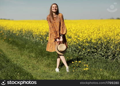 beautiful young woman walks in a field of yellow rapeseed. Girl brunette long hair fly in wind dressed in dress and straw hat. summer holiday concept.. beautiful young woman walks in a field of yellow rapeseed. Girl brunette long hair fly in wind dressed in dress and straw hat. summer holiday concept