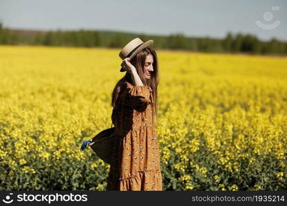 beautiful young woman walks in a field of yellow rapeseed. Girl brunette long hair fly in wind dressed in dress and straw hat. summer holiday concept.. beautiful young woman walks in a field of yellow rapeseed. Girl brunette long hair fly in wind dressed in dress and straw hat. summer holiday concept