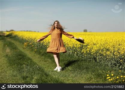 beautiful young woman walks in a field of yellow rapeseed. Girl brunette long hair fly in wind dressed in dress and straw hat. summer holiday concept.. beautiful young woman walks in a field of yellow rapeseed. Girl brunette long hair fly in wind dressed in dress and straw hat. summer holiday concept