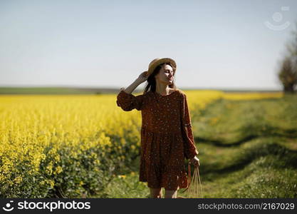 beautiful young woman walks in a field of yellow rapeseed. Girl brunette long hair fly in wind dressed in dress and straw hat. summer holiday concept.. beautiful young woman walks in a field of yellow rapeseed. Girl brunette long hair fly in wind dressed in dress and straw hat. summer holiday concept