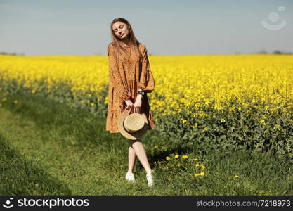 beautiful young woman walks in a field of yellow rapeseed. Girl brunette long hair fly in wind dressed in dress and straw hat. summer holiday concept.. beautiful young woman walks in a field of yellow rapeseed. Girl brunette long hair fly in wind dressed in dress and straw hat. summer holiday concept