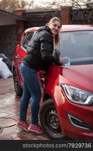 Beautiful young woman washing red car