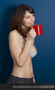 Beautiful young woman wearing a casual lingerie against a blue wall, and drinking coffee