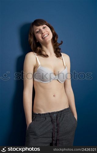 Beautiful young woman wearing a casual lingerie and pajama pants, against a blue wall