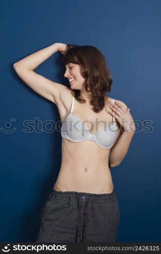 Beautiful young woman wearing a casual lingerie and pajama pants, against a blue wall