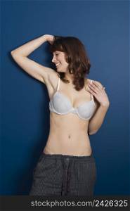 Beautiful young woman wearing a casual lingerie and pajama pants, against a blue wall