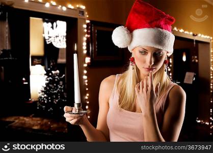 beautiful young woman wearing a christmas hat and keeping a candle in a dark contest