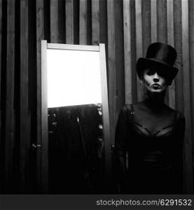 Beautiful young woman wearing a high hat near the mirror . Retro style