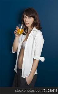 Beautiful young woman wearing a pajama against a blue wall, and drinking a orange juice
