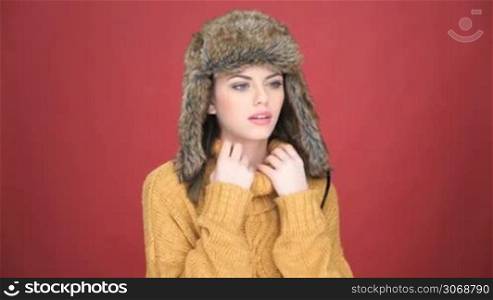 Beautiful young woman wearing a warm fur hat suffering from the cold frowning as she snuggles down into the polo neck of her warm jersey