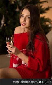 Beautiful young woman wearing Christmas sweater with deers ornament sitting on sofa near Christmas Tree