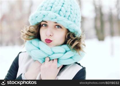 Beautiful young woman wearing merino wool pastel colors hat and scarf enjoying the fresh morning outdoors. Skin Care, Lip care, care of the eyelashes in the winter season.