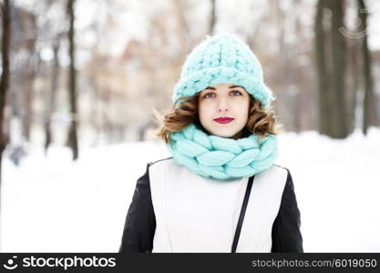 Beautiful young woman wearing merino wool pastel colors hat and scarf enjoying the fresh morning outdoors. Skin Care, Lip care, care of the eyelashes in the winter season.