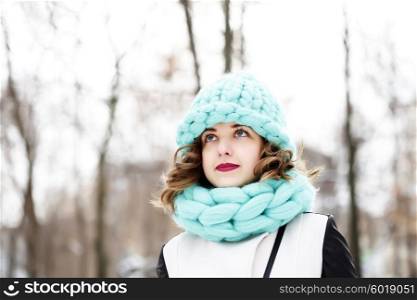 Beautiful young woman wearing merino wool pastel colors hat and scarf enjoying the fresh morning outdoors. Skin Care, Lip care, care of the eyelashes in the winter season.