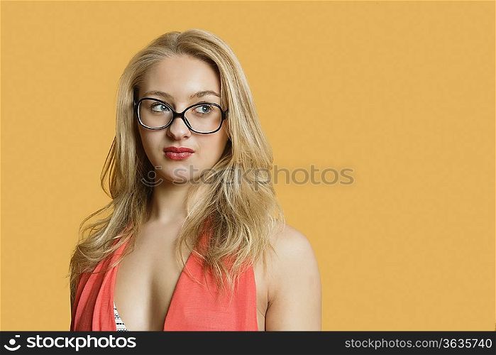 Beautiful young woman wearing retro glasses looking away over colored background