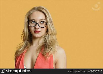 Beautiful young woman wearing retro glasses looking away over colored background