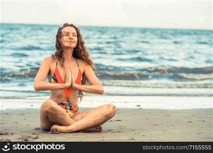 Beautiful young woman wearing swimsuit is on summer vacation. Travel and lifestyle.. Young woman practices yoga on the beach in summer.