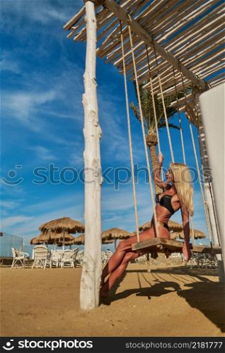 Beautiful young woman wearing swimsuit swinging on a swing during sunny day at resort.. Beautiful young woman wearing swimsuit swinging on a swing during sunny day at resort