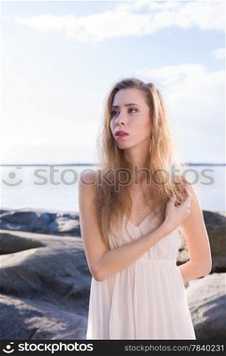 Beautiful young woman wearing white dress, scandinavian shore and sea on background
