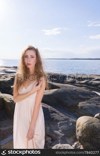 Beautiful young woman wearing white dress, scandinavian shore and sea on background