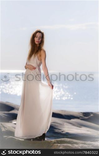 Beautiful young woman wearing white dress, scandinavian shore and sea on background