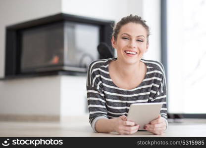 beautiful young woman websurfing using tablet computer on the floor in front of fireplace on cold winter day at home