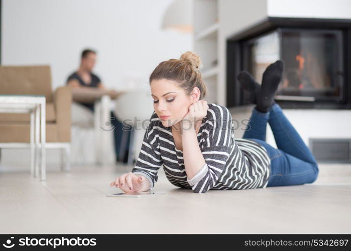 beautiful young woman websurfing using tablet computer on the floor in front of fireplace on cold winter day at home