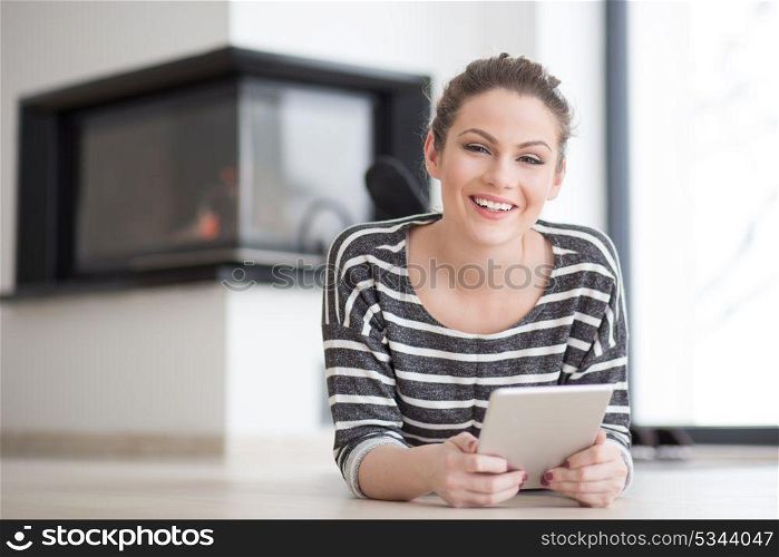 beautiful young woman websurfing using tablet computer on the floor in front of fireplace on cold winter day at home