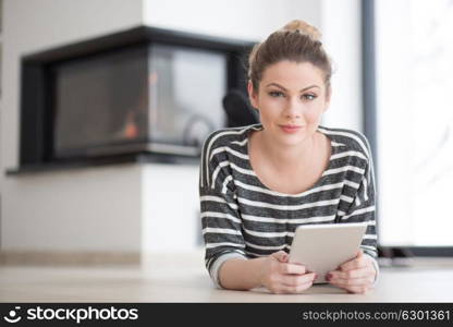 beautiful young woman websurfing using tablet computer on the floor in front of fireplace on cold winter day at home