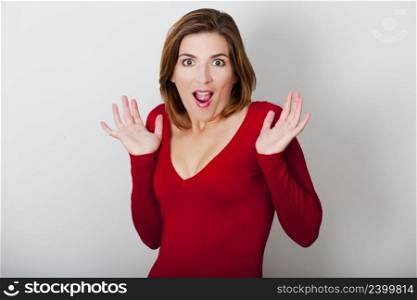 Beautiful young woman with a astonished expression, against a gray wall