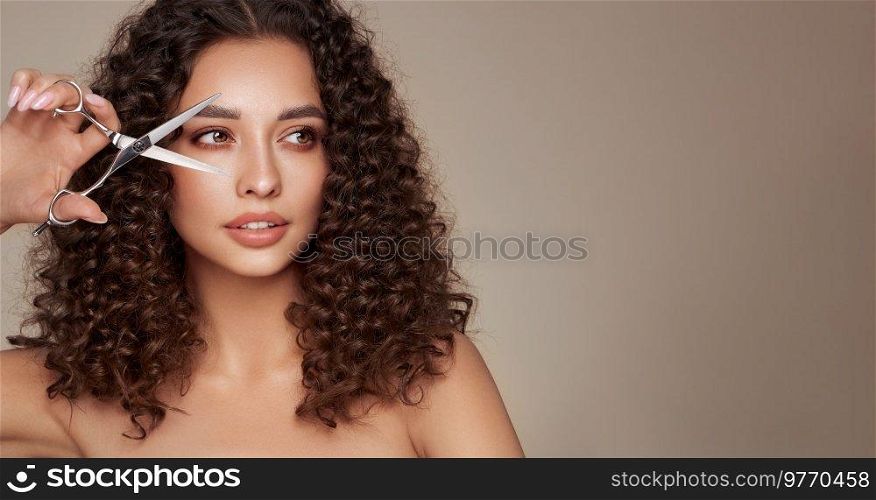 Beautiful young woman with a bright makeup and a afro  hair holds metal scissors. Model with curly hair. Hair salon, haircut. Care and beauty hair products. Perfect make-up