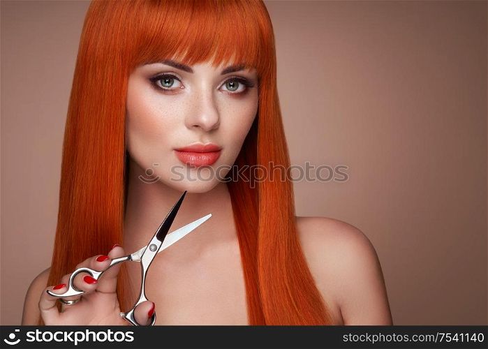 Beautiful young woman with a bright makeup and a smooth long hair holds metal scissors. Model with red hair. Hair salon, haircut. Care and beauty hair products. Perfect make-up