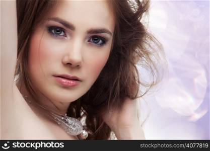 Beautiful young woman with a necklace on sparkling pink background, touching her hair