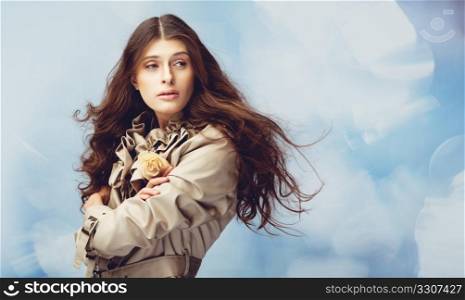 Beautiful young woman with a rose on sparkling blue background, her hair fly on the wind, springtime.