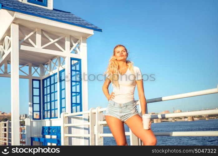 Beautiful young woman with a take away coffee cup, standing on the bridge near the water.