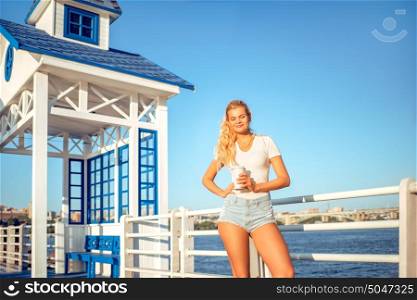 Beautiful young woman with a take away coffee cup, standing on the bridge near the water.