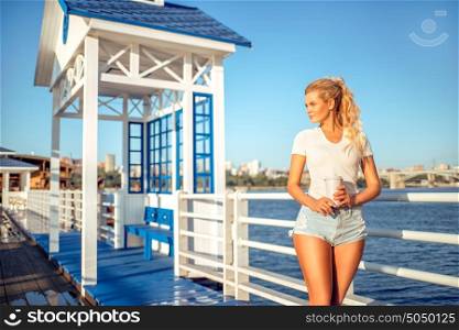 Beautiful young woman with a take away coffee cup, standing on the bridge near the water.