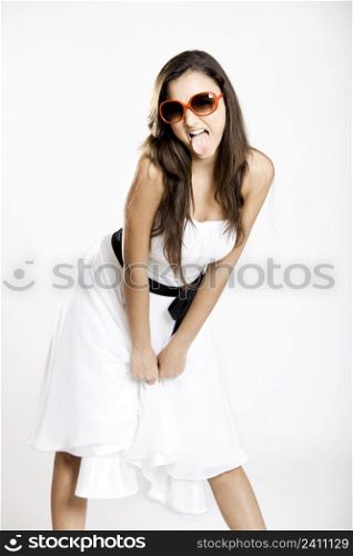 Beautiful young woman with a white dress and sunglasses showing her tongue out