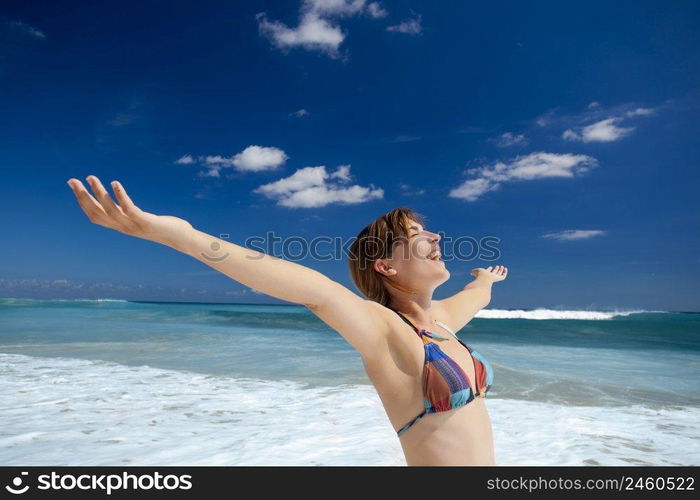 Beautiful young woman with arms open in a tropical beach enjoying the summer 