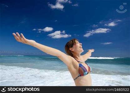 Beautiful young woman with arms open in a tropical beach enjoying the summer 
