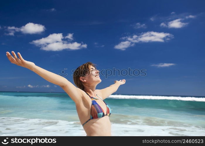 Beautiful young woman with arms open in a tropical beach enjoying the summer